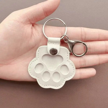 Llavero portátil multifuncional con diseño de huella de gato, fabricado en cuero, con compartimento para guardar pelo o recuerdos de mascotas.